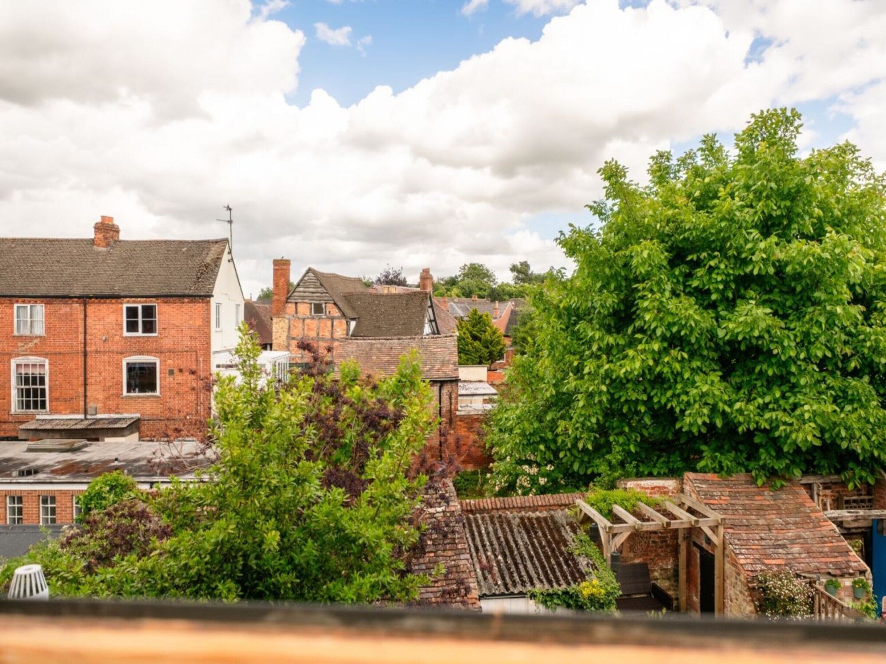 A traditional brick building with a sloped roof, surrounded by lush greenery and other residential structures.