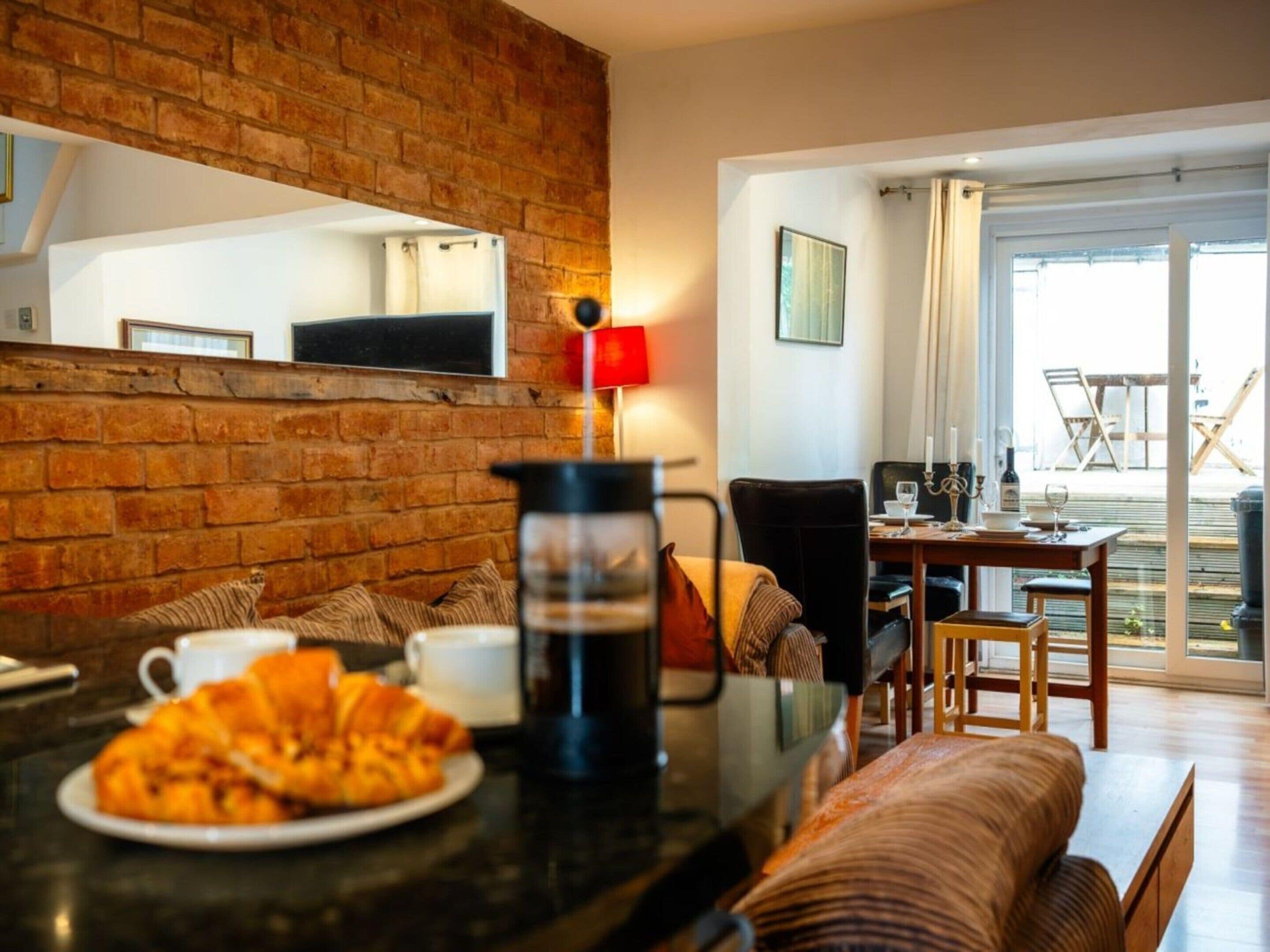 A cozy living area with a brick wall, a coffee table with pastries, a sofa, and a dining table with chairs.