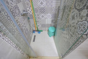 A bathroom with patterned tiles, a green plastic stool, and a broom leaning against the wall. - Cosy Appartement 2 Chambres Avec Balcon à Corniche (Martil)