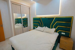 A bedroom with a bed, bedside tables, a mirror, and a wardrobe. - Cosy Appartement 2 Chambres Avec Balcon à Corniche (Martil)