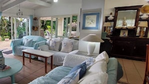A living room with a sofa set, a coffee table, and a lamp. There is a large window with a view of greenery outside.