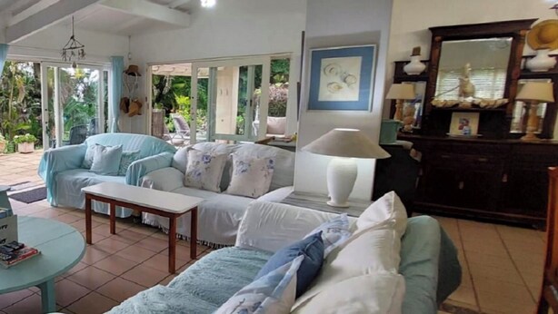 A living room with a sofa set, a coffee table, and a lamp. There is a large window with a view of greenery outside.