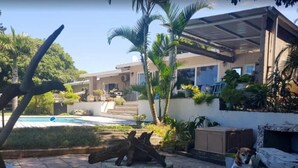 A pool area with a wooden bench, a dog, and a house with a covered patio.