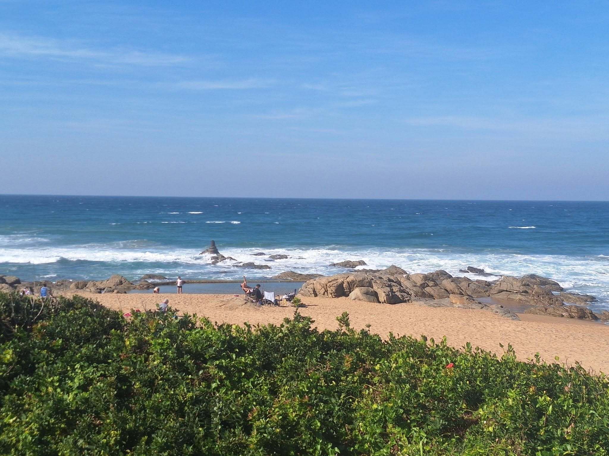 A beach with rocky outcrops, clear blue sky, and calm sea.