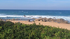 A beach with rocky outcrops, clear blue sky, and calm sea.