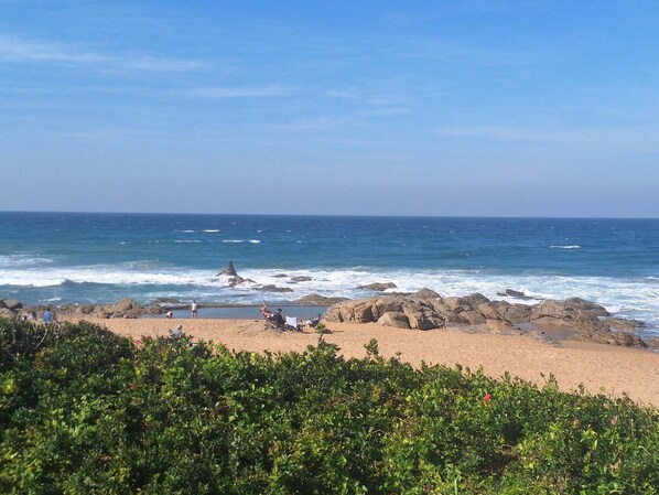 A beach with rocky outcrops, clear blue sky, and calm sea.