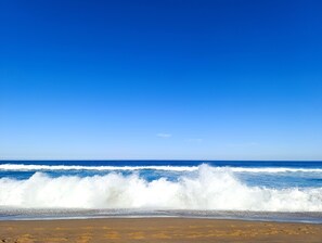 A beach with waves crashing onto the shore under a clear blue sky.