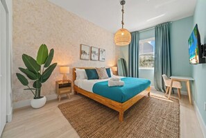 A bedroom with a bed, bedside table, lamp, potted plant, and a view of the outdoors.