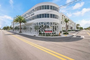 A modern building with a curved facade, a sign for 'AUSTRO AVAILABLE' with a phone number, and palm trees in the foreground.