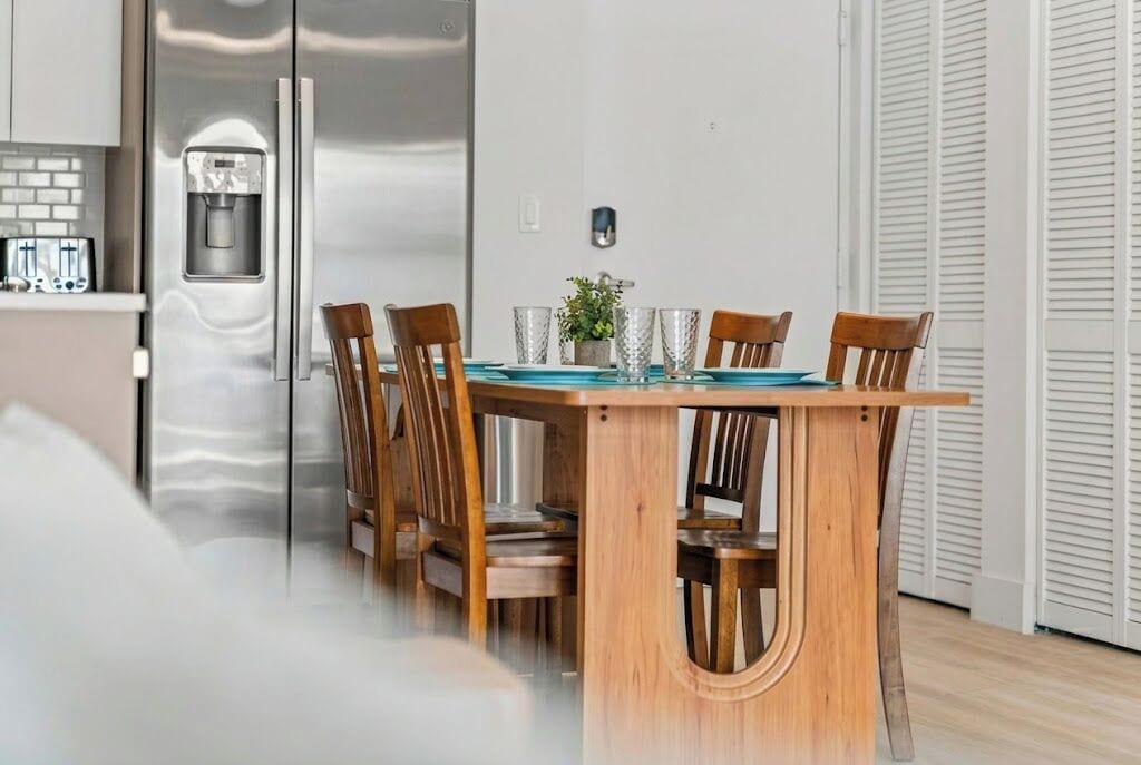 Een moderne keuken met een ingebouwde waterdispenser, een eettafel met stoelen en een potplant aan de wand.