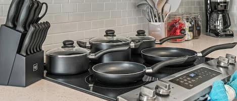 A kitchen with a stove, pots, pans, a knife block, and a coffee maker.