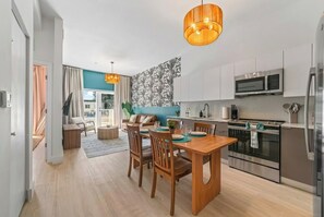 A modern kitchen with stainless steel appliances, a dining area with wooden furniture, and a view to the outside.