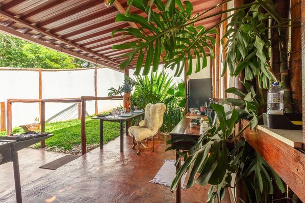 An outdoor patio with a wooden table, a cushioned chair, and various plants.