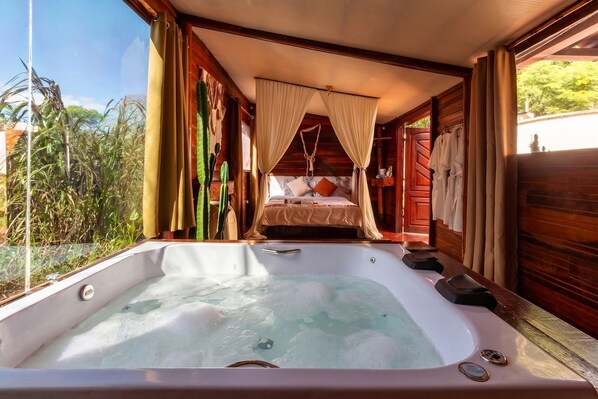 A room with a large hot tub, a bed with a canopy, and a view of greenery outside.