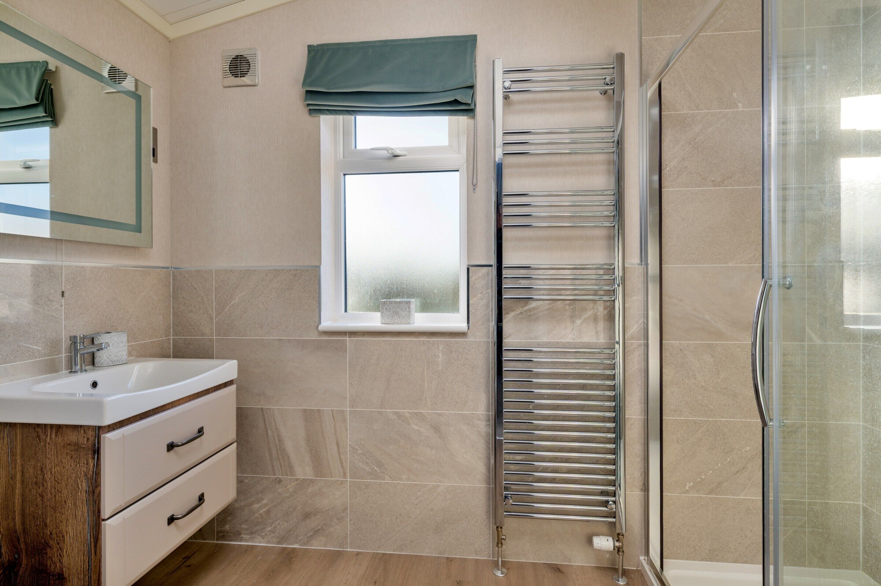 A bathroom with a shower, a sink with a mirror, and a window with a curtain.