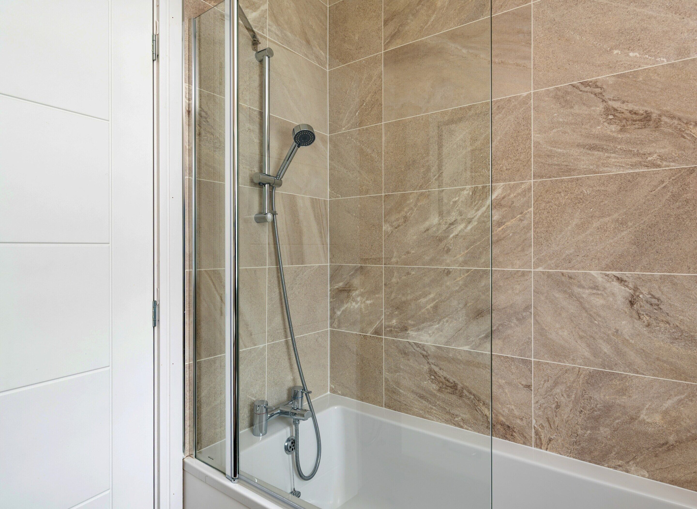 A shower with a glass door, a handheld showerhead, and a handheld shower attachment.