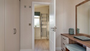 Quarto com toucador de madeira, um espelho e uma porta que dá para uma casa de banho com um suporte para toalhas.