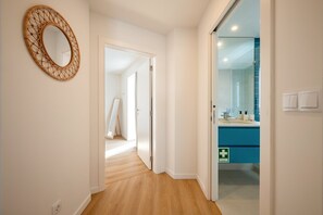 A hallway with a mirror, a door leading to a bathroom, and a wooden floor. - GuestReady - Riverside Retreat (Alcochete)