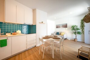 A modern kitchen with white cabinets, a blue backsplash, and a dining area with a round table and chairs. - GuestReady - Riverside Retreat (Alcochete)