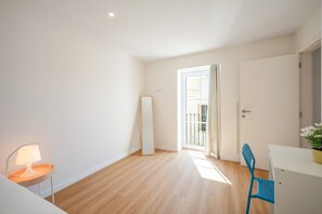 A room with a wooden floor, a white door, a blue chair, and a white desk. - GuestReady - Riverside Retreat (Alcochete)