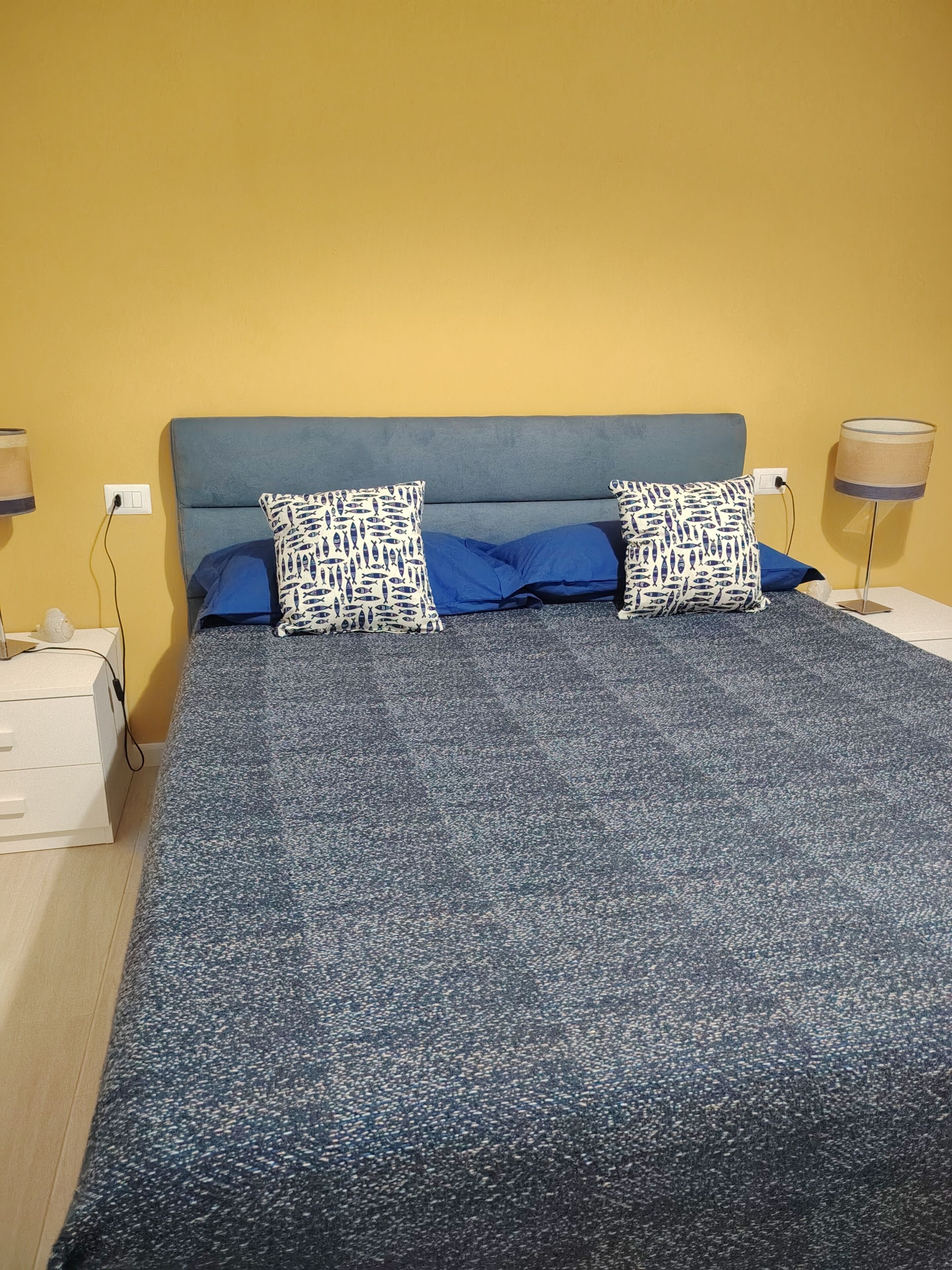A bed with a blue headboard, two pillows with a fish pattern, and a blue blanket.