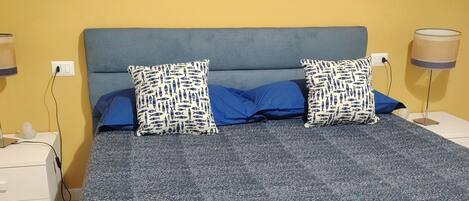 A bed with a blue headboard, two pillows with a fish pattern, and a blue blanket.