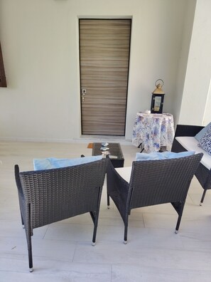 A patio area with wicker furniture, a table with a floral tablecloth, and a door in the background.