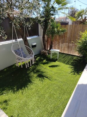 A backyard with artificial grass, a white swing chair, a small white table, and a wooden fence.