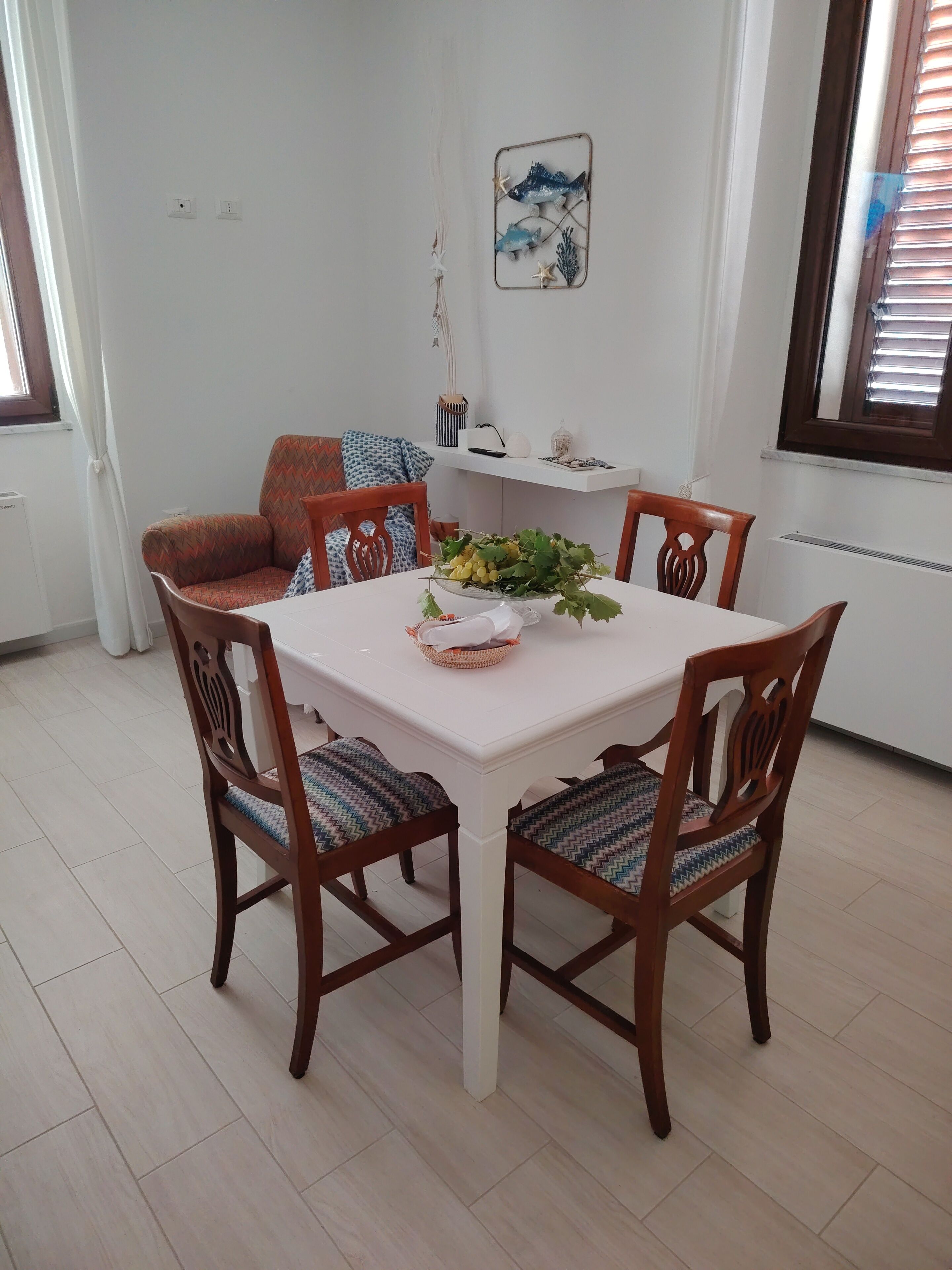 Un comedor con una mesa blanca, cuatro sillas de madera y un adorno en la pared.