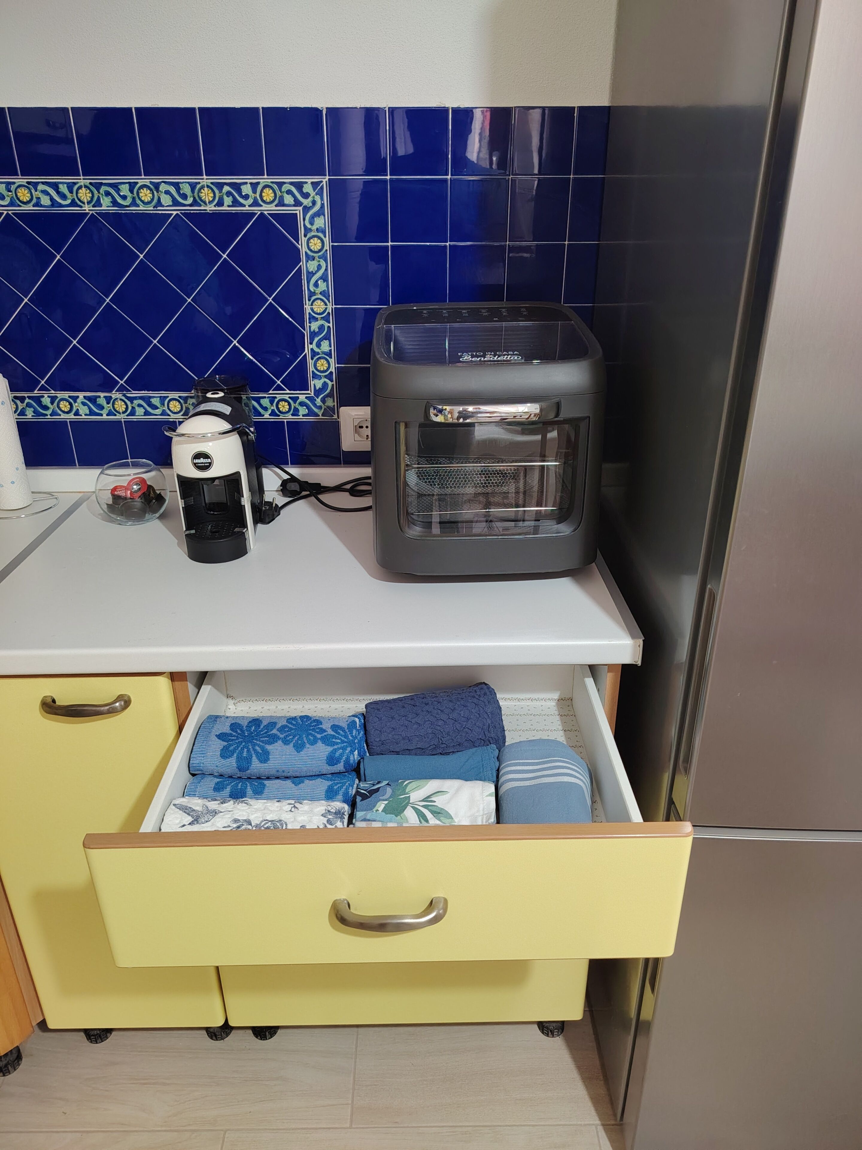 A kitchen with a coffee maker, a toaster, and a microwave on the counter. There is a yellow drawer with folded towels.