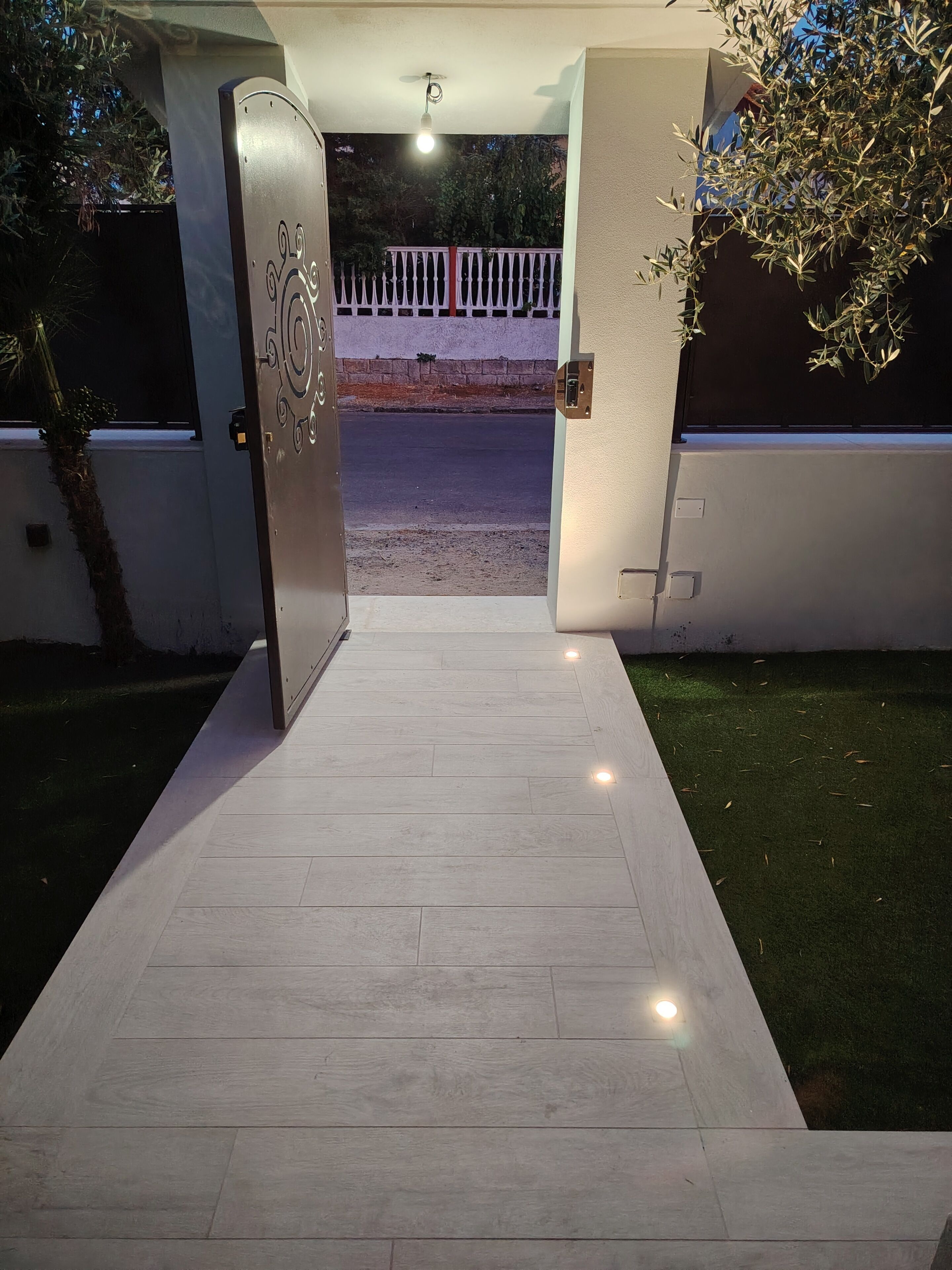 Una entrada con puerta y un camino iluminado que conduce a la calle.