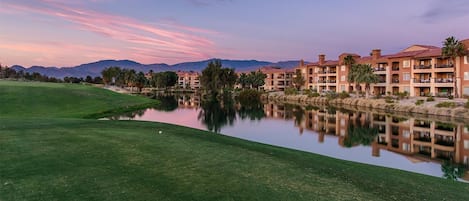 Un parcours de golf avec un plan d’eau qui reflète les bâtiments et les montagnes en arrière-plan.