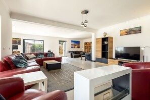 A modern living room with a red leather sofa, a white coffee table, and a TV. There is a bookshelf and a painting on the wall. - Luxurious Retreat in Lousã Countryside (Lagarteira)