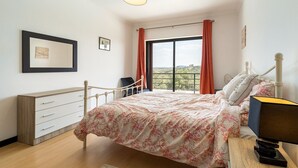 Een slaapkamer met een bed, een bureau, een stoel, een raam met gordijnen en een hanglamp.