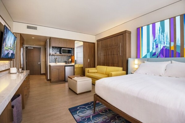 A hotel room with a bed, a sofa, a desk, a kitchenette, and a bathroom.