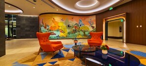 A lobby with two orange armchairs, a glass coffee table, and a colorful mural on the wall.