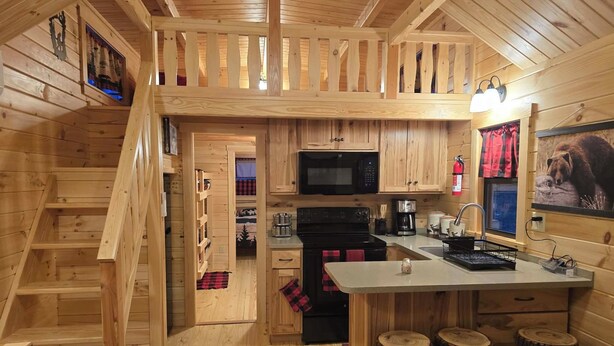Interior de uma cabana de madeira, com cozinha, sala de jantar e escada.