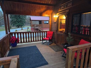 Eine Holzterrasse mit einem roten Stuhl und einem kleinen Tisch, einer blauen Matte und Blick auf eine Hütte mit rotem Dach.