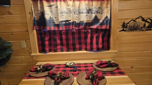 Interior de uma cabana de madeira com uma mesa posta para dois, com toalhas de mesa xadrez e guardanapos xadrez vermelho e preto.