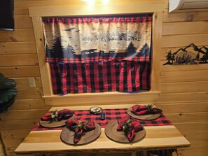 Ein Holzblockhaus-Interieur mit einem für zwei Personen gedecktem Tisch, ausgestattet mit karierten Tischdecken und roten sowie schwarzen Karottenervilten.