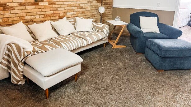 A room with a brick wall, a sofa, a chair, a small table, and a lamp. - Perfect Downtown Location in Mount Pleasant with AC (Mount Pleasant)