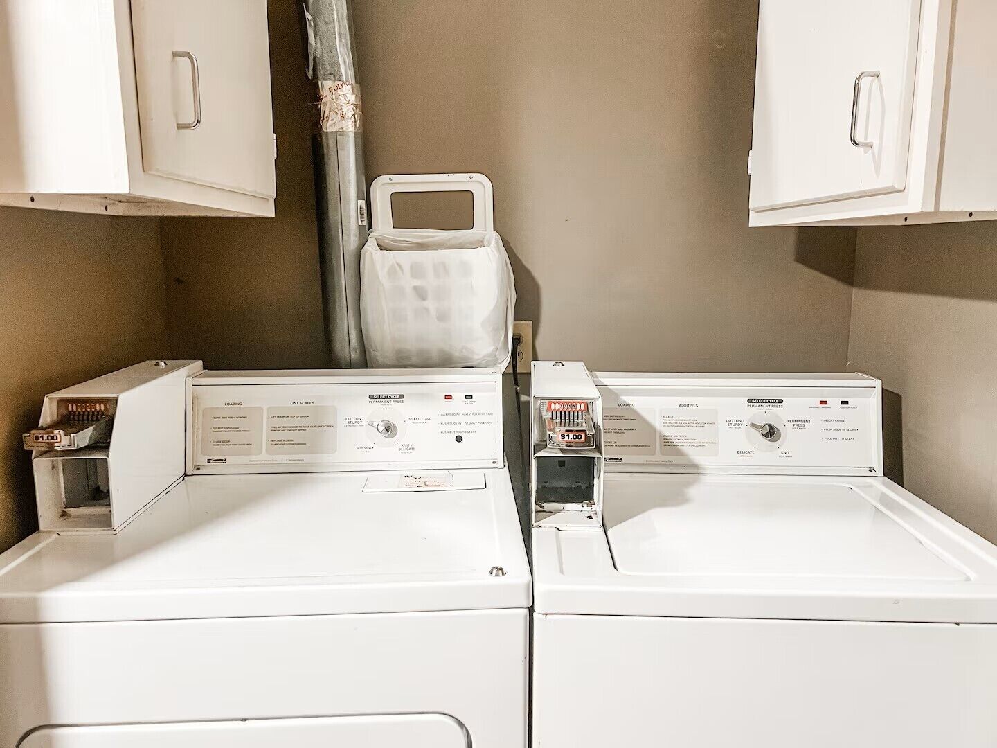 A laundry room with two front-loading washing machines and cabinets above them.