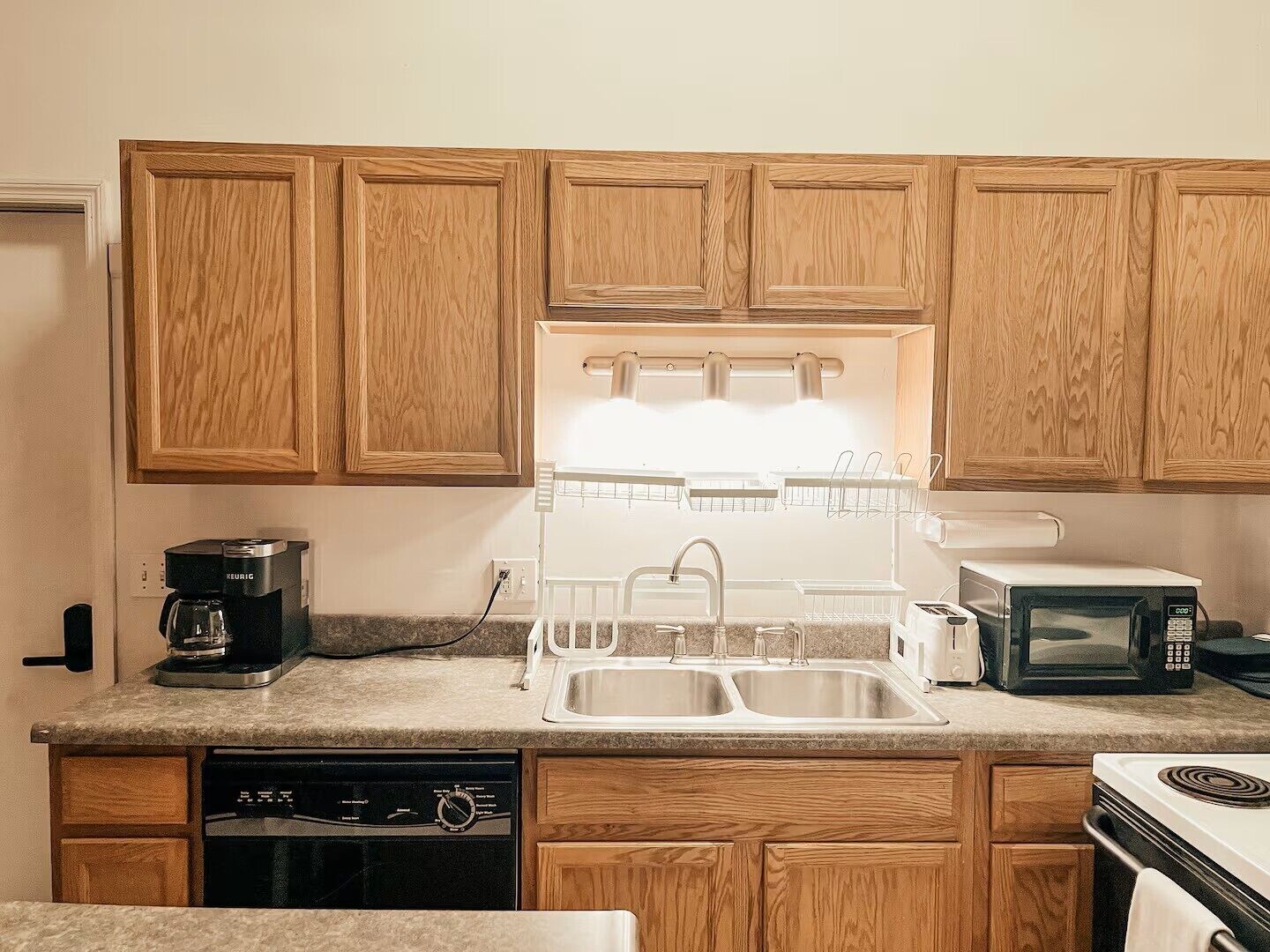 A kitchen with wooden cabinets, a built-in dishwasher, a coffee maker, a sink, a microwave, and a toaster.