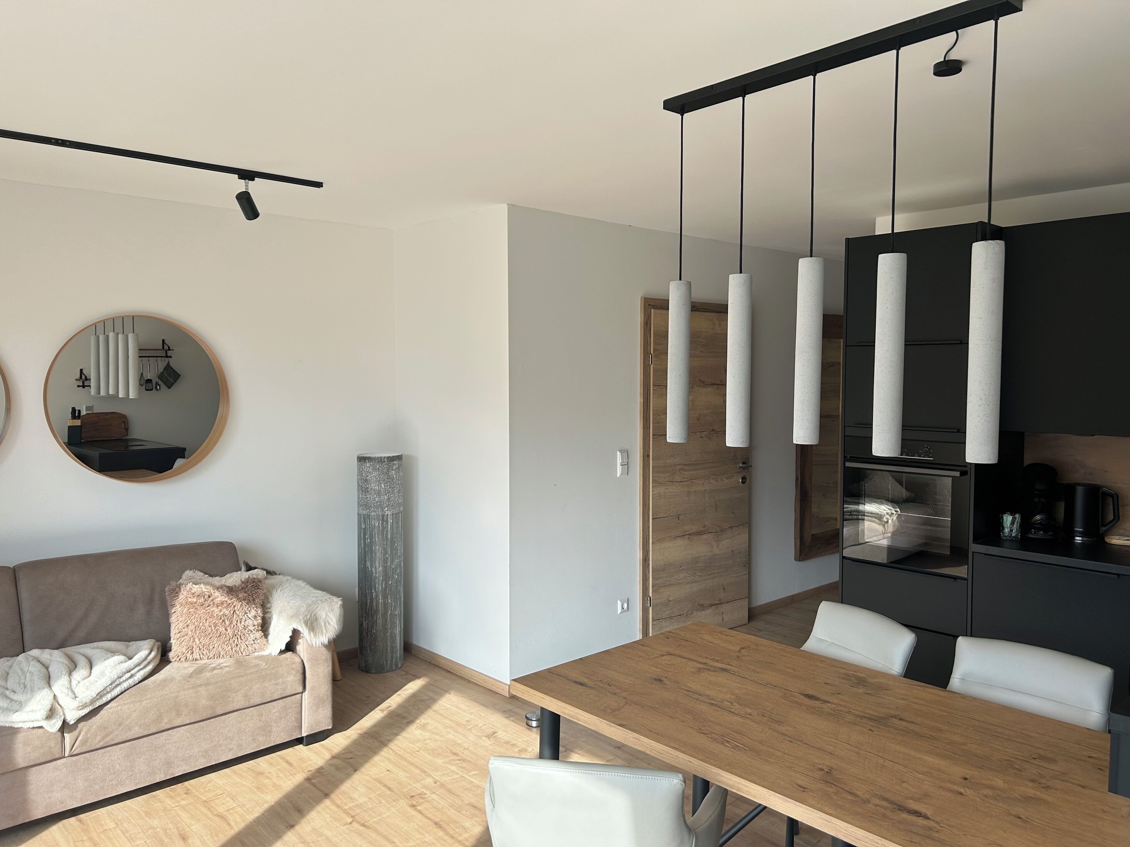 Un salon moderne avec une table à manger en bois, un canapé et un coin cuisine agrémenté de luminaires suspendus.