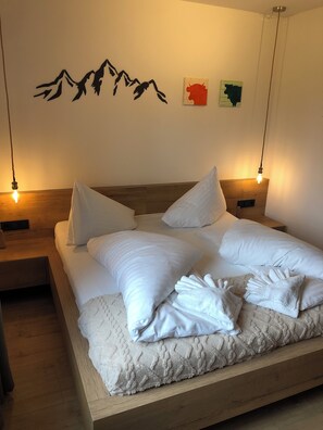 A neatly made bed with white linens and a fluffy blanket, two bedside tables with lamps, and wall art depicting mountains and a bull. - About Stella – Modern "Nassfeld" Vacation Rental on Lake Pressegger & Nassfeld (Presseggen)