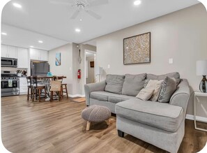 A modern living room with a grey sofa, ottoman, and a dining area with a table and chairs.
