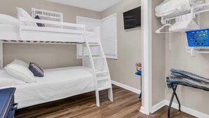 Camera con letto a castello, scaletta, televisore montato a parete e angolo lavanderia con cesto e asse da stiro.