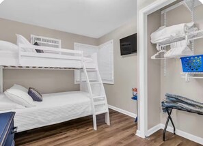 A bunk bed room with a ladder, a TV mounted on the wall, and a laundry area with a basket and ironing board. - Seaside Cottage - a guest favorite since 2021! (Seaside Heights)