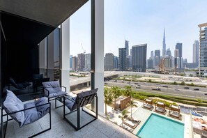 A balcony with a pool, lounge chairs, and a city view. - Modern Upside Studio w/ Skyline View (Dubai)