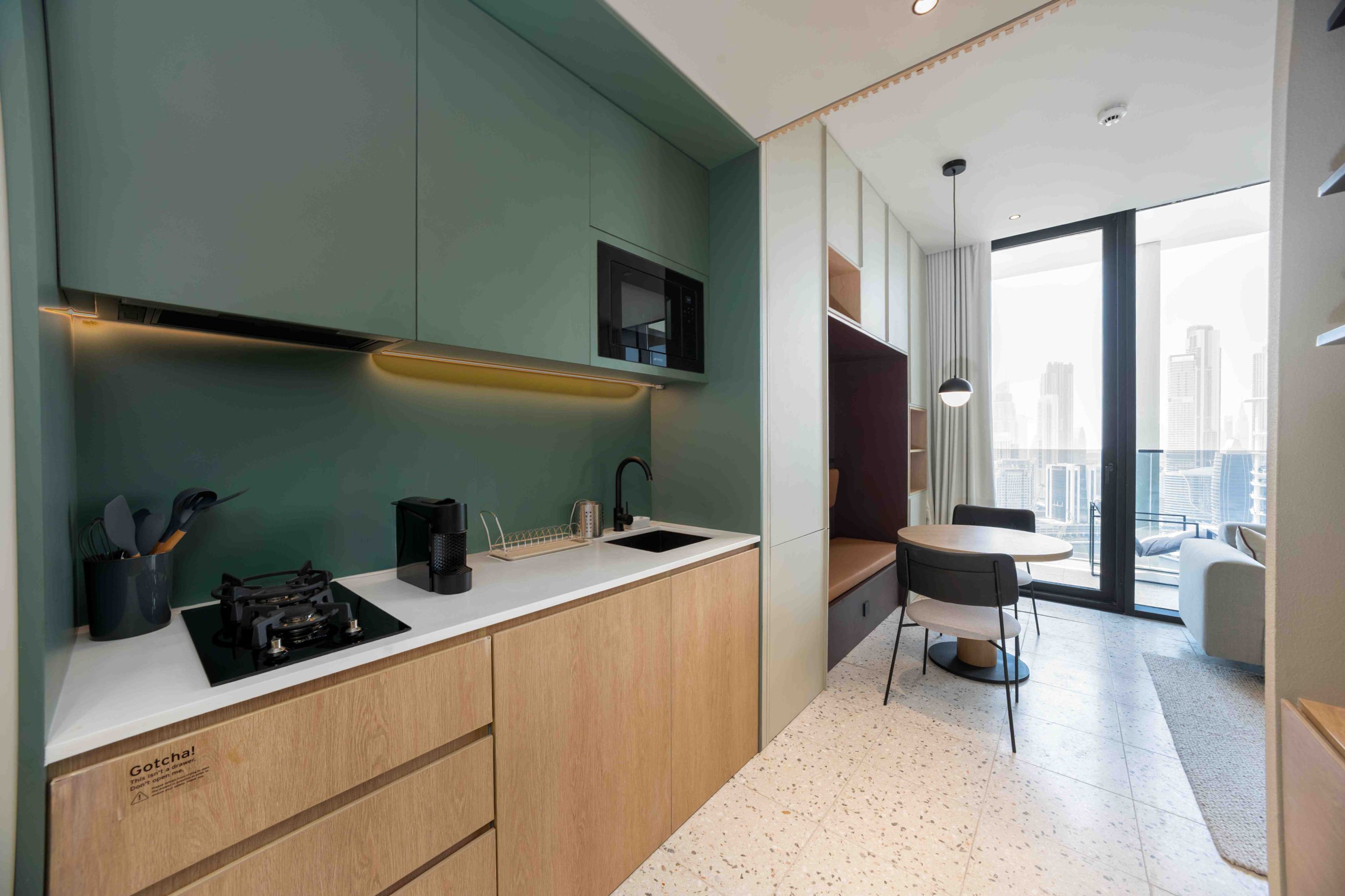 Eine moderne Küche mit Einbauherd, Spüle und Kaffeemaschine. Ein Essbereich mit Tisch und Stühlen lädt zum Verweilen ein, und große Fenster bieten einen Blick auf die Stadt.